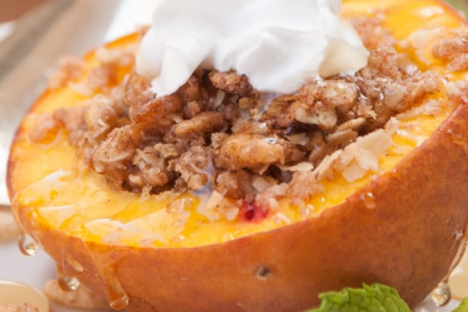 A bake peach cut in half with the seed removed. Inside is granola and honey topped with whipped cream.