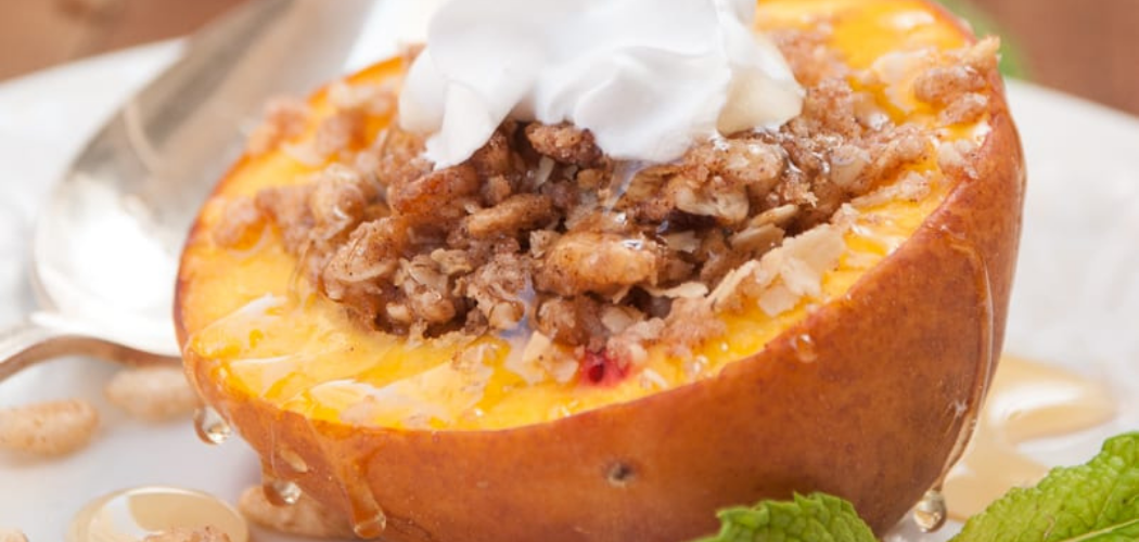 A bake peach cut in half with the seed removed. Inside is granola and honey topped with whipped cream.