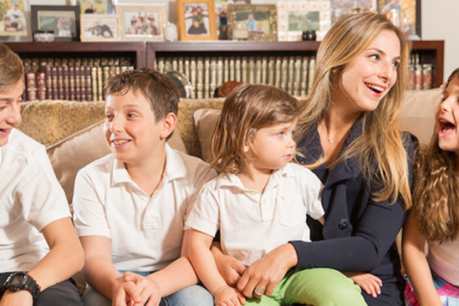 Busy moms sits with her three sons and daughter laughing on a couch.