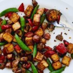 Plate of golden tofu with green sugarsnap peas and red peppers