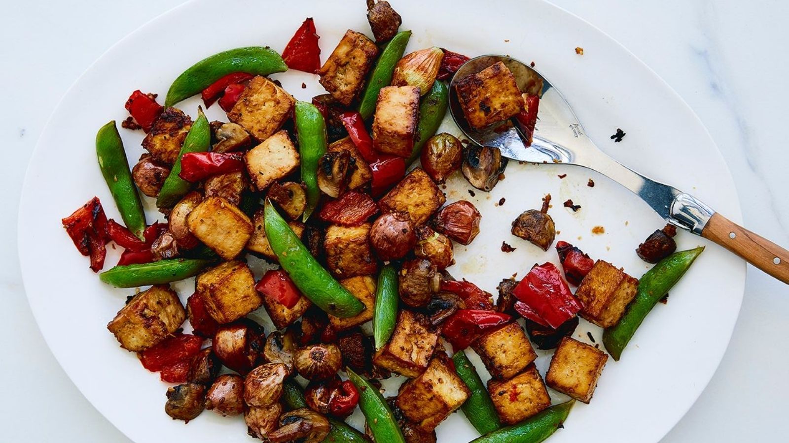Plate of golden tofu with green sugarsnap peas and red peppers