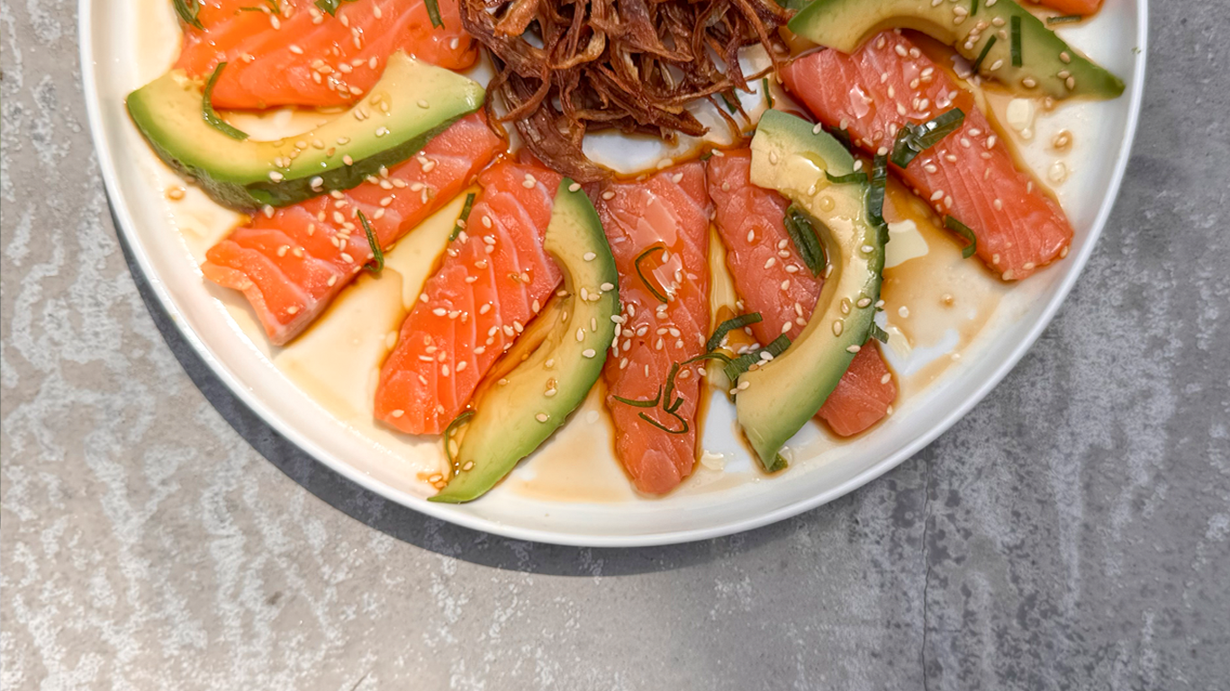 Salmon sashimi slices with avocado, sesame seeds, soy sauce, and shredded red cabbage on a white plate