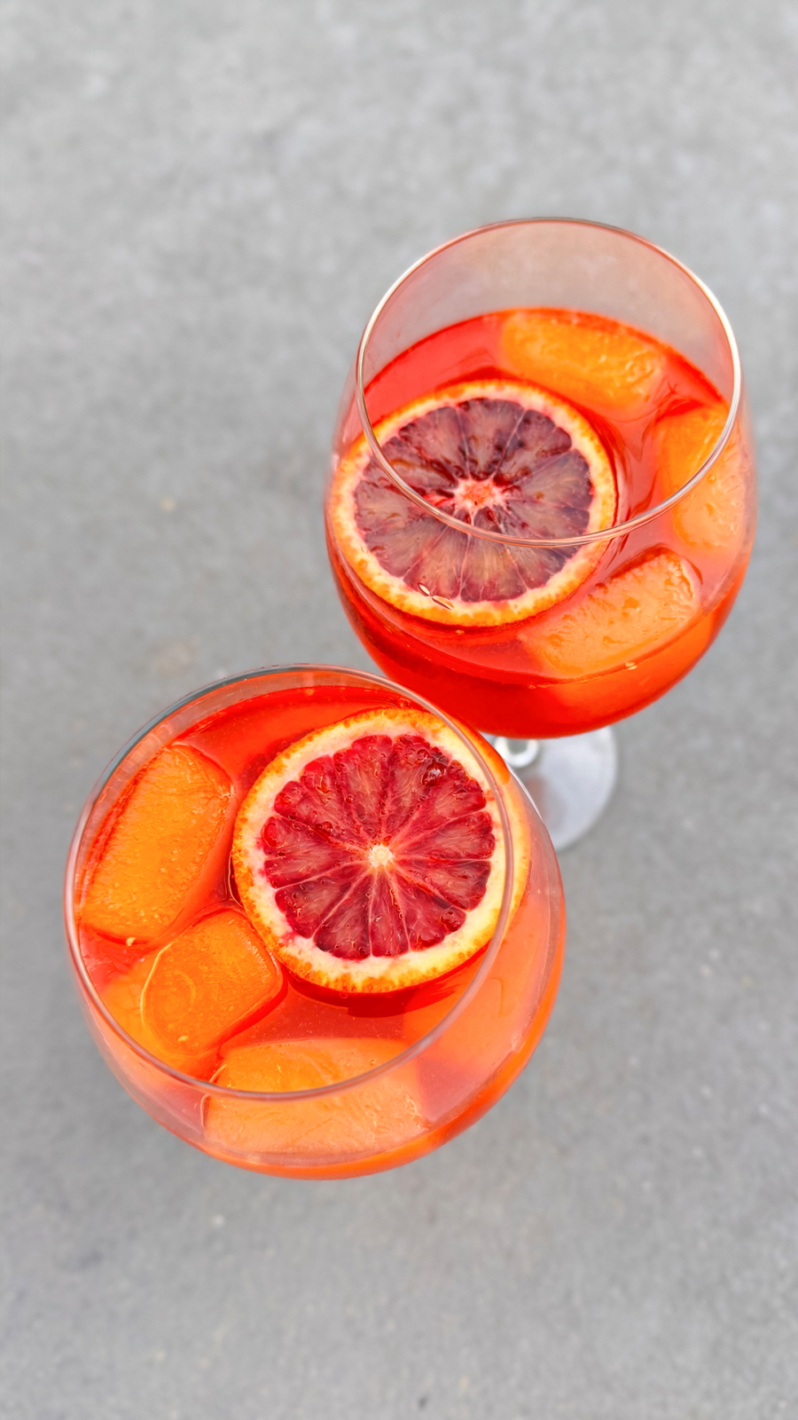 Orange-Spiked Aperol Spritz served with blood orange slices and frozen orange juice cubes in a wine glass