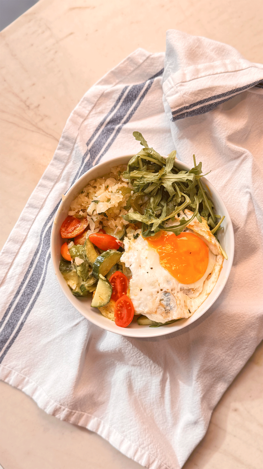 Cilantro Lime Cauliflower Rice bowl with arugula, avocado, tomatoes, and fried eggs on top, drizzled with green dressing