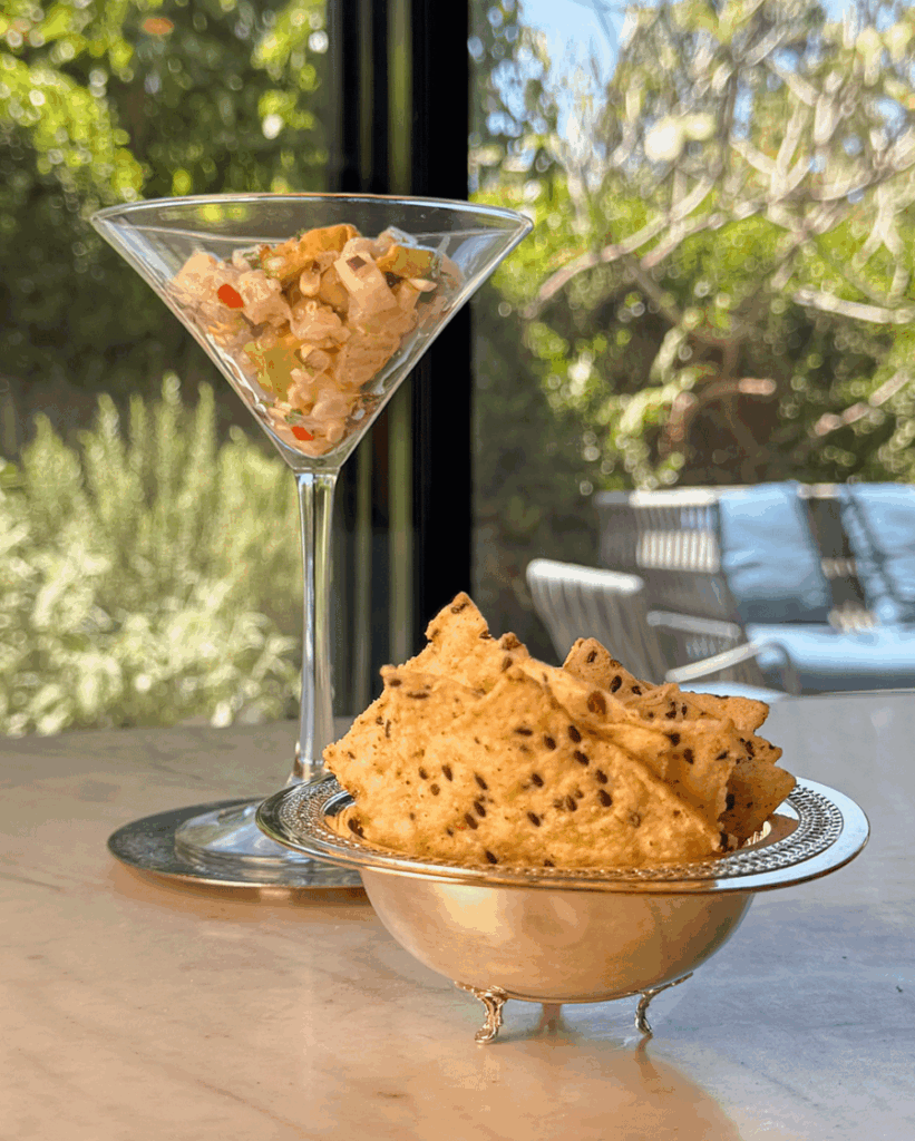 A martini glass of yellowtail ceviche salad with a silver bowl of seeded chips in front, styled for outdoor summer entertaining