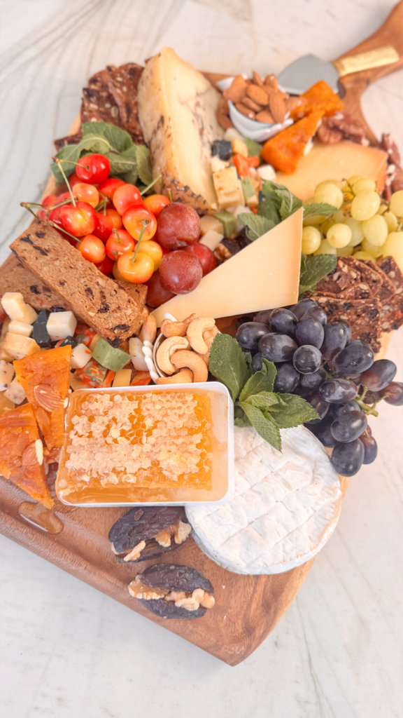 Close-up of a dessert cheeseboard with honeycomb, brie, grapes, dates, brittle, and mixed cheeses on a wooden board