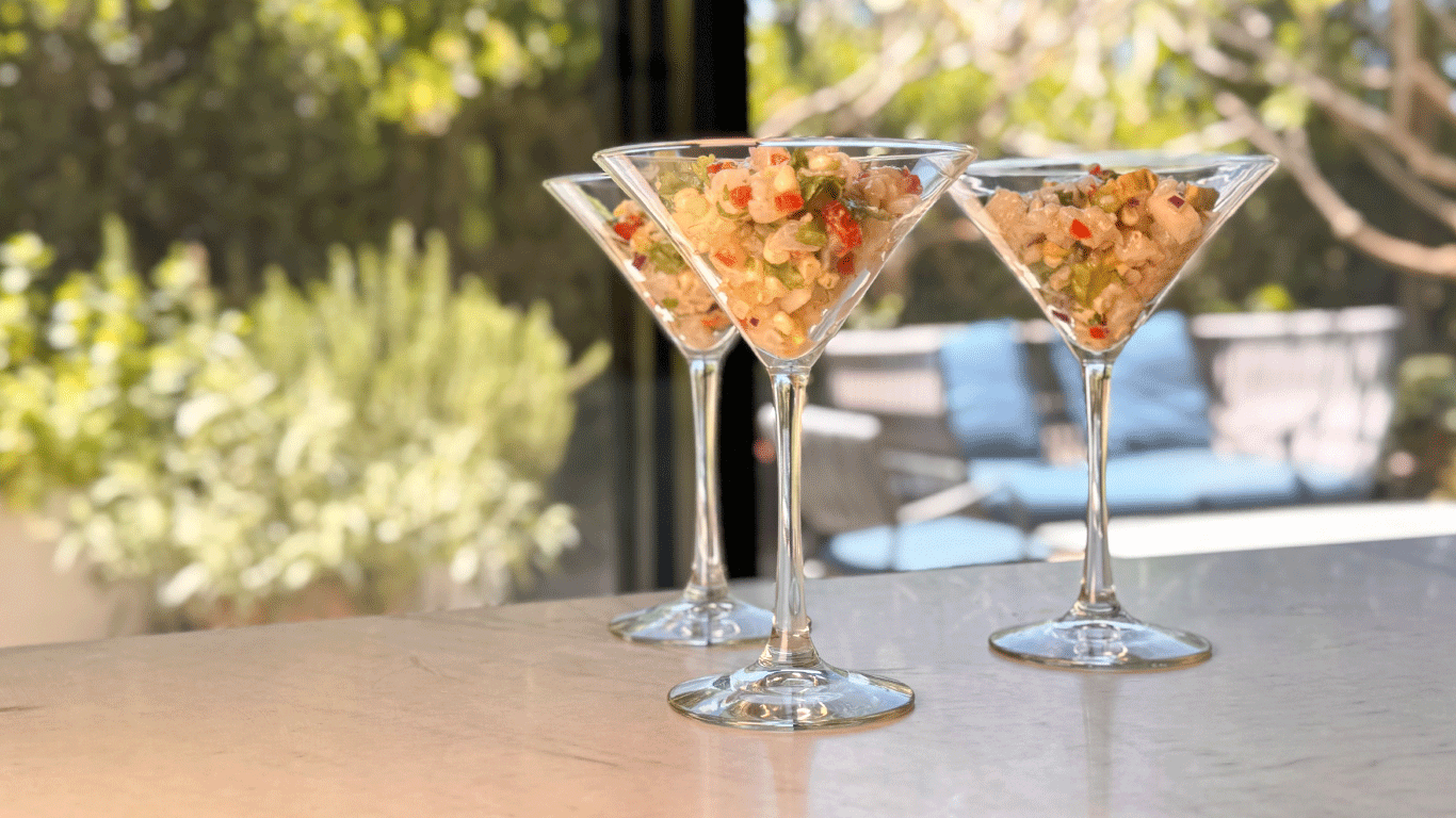 Three martini glasses filled with ceviche salad made with yellowtail, avocado, corn, jicama, and lime, served on a sunlit table