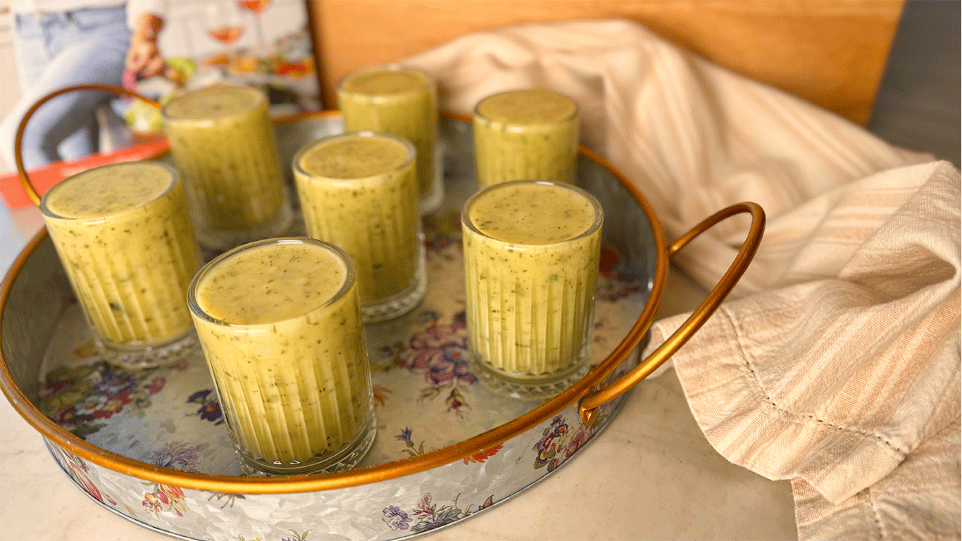 Creamy zucchini soup served in small glasses on a floral tray, ideal for entertaining or an elegant starter