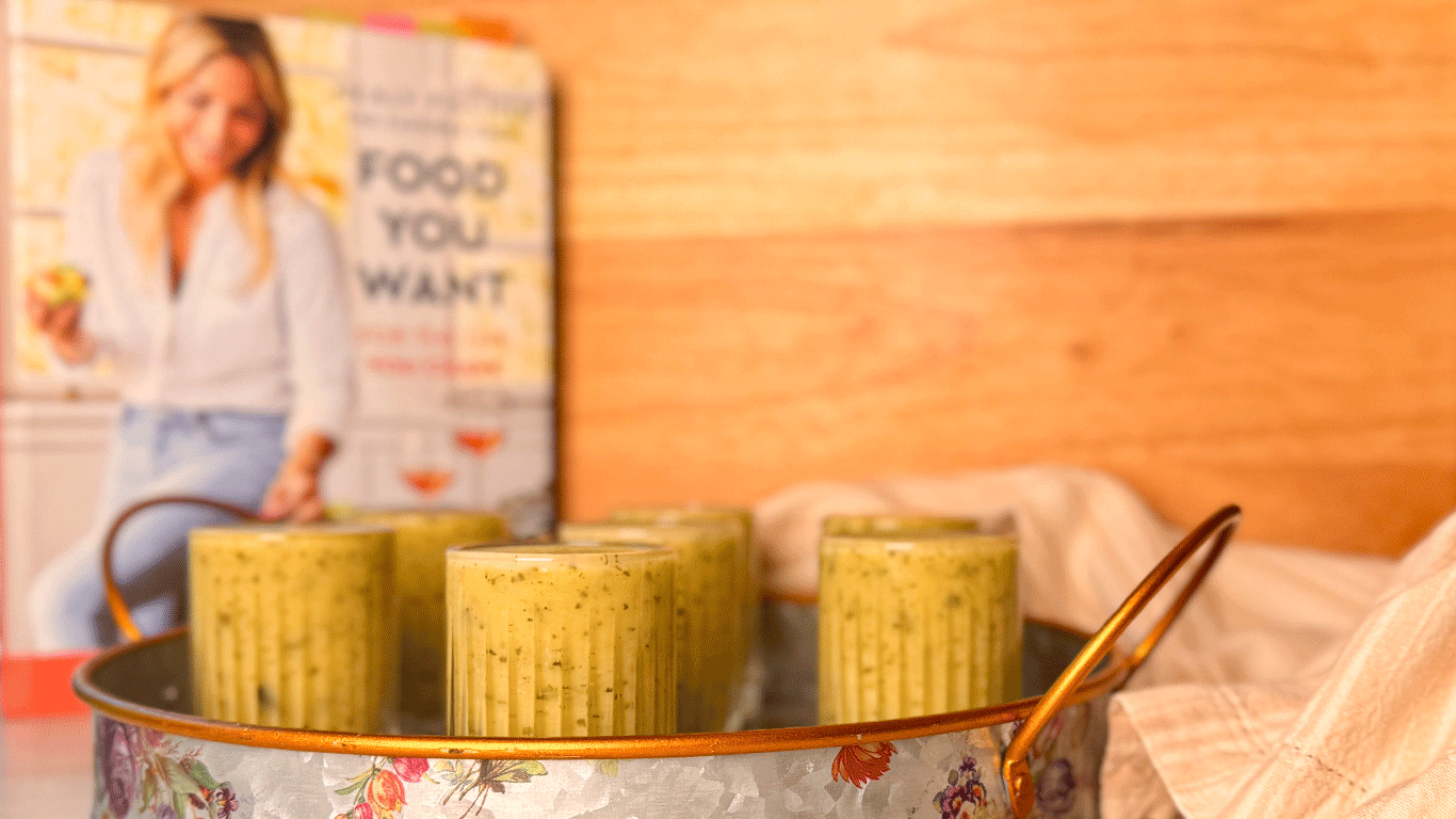 Creamy zucchini soup served in small glasses on a tray with the Food You Want cookbook in the background
