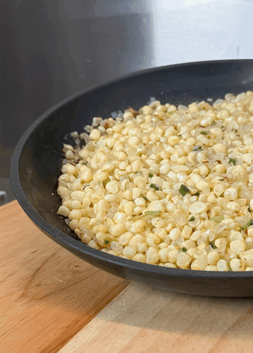 Buttered sweet corn off the cob cooking in a skillet with onions and scallions