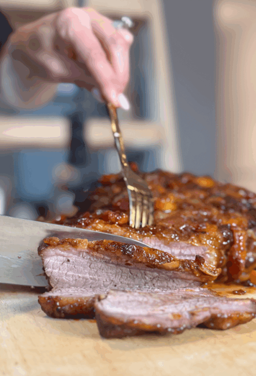 Close-up of sliced brisket being cut with a knife and fork, topped with caramelized sauce