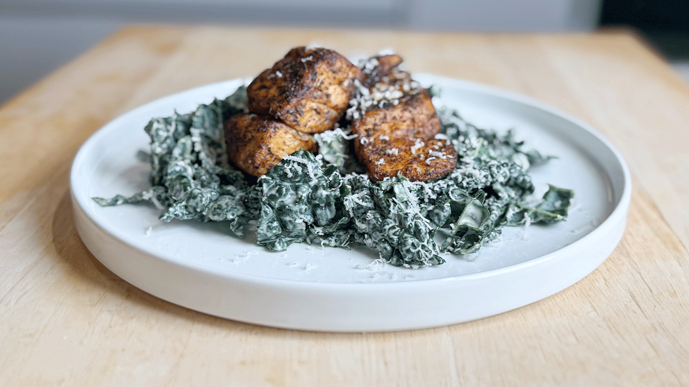 Plate of blackened sea bass served over kale salad with creamy vegan Caesar dressing and grated Parmesan on a white ceramic dish