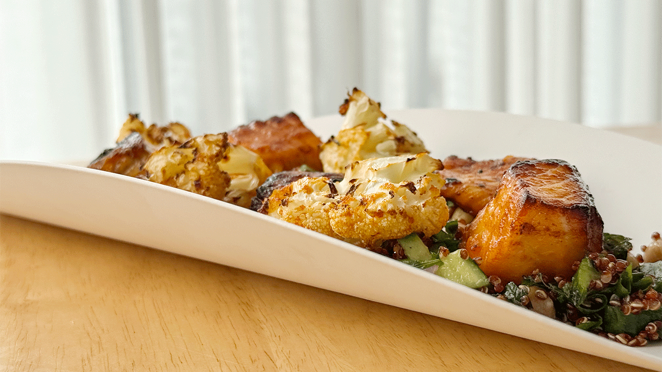 Crispy air-fried salmon and roasted cauliflower served over fresh greens and quinoa in a white bowl.