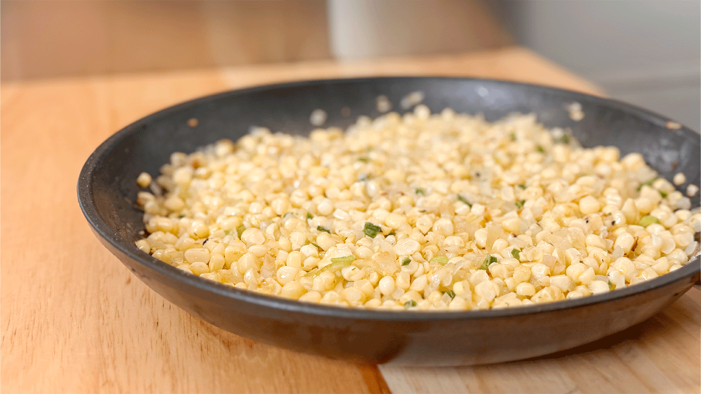 Skillet filled with buttered sweet corn off the cob, sautéed with onions and herbs