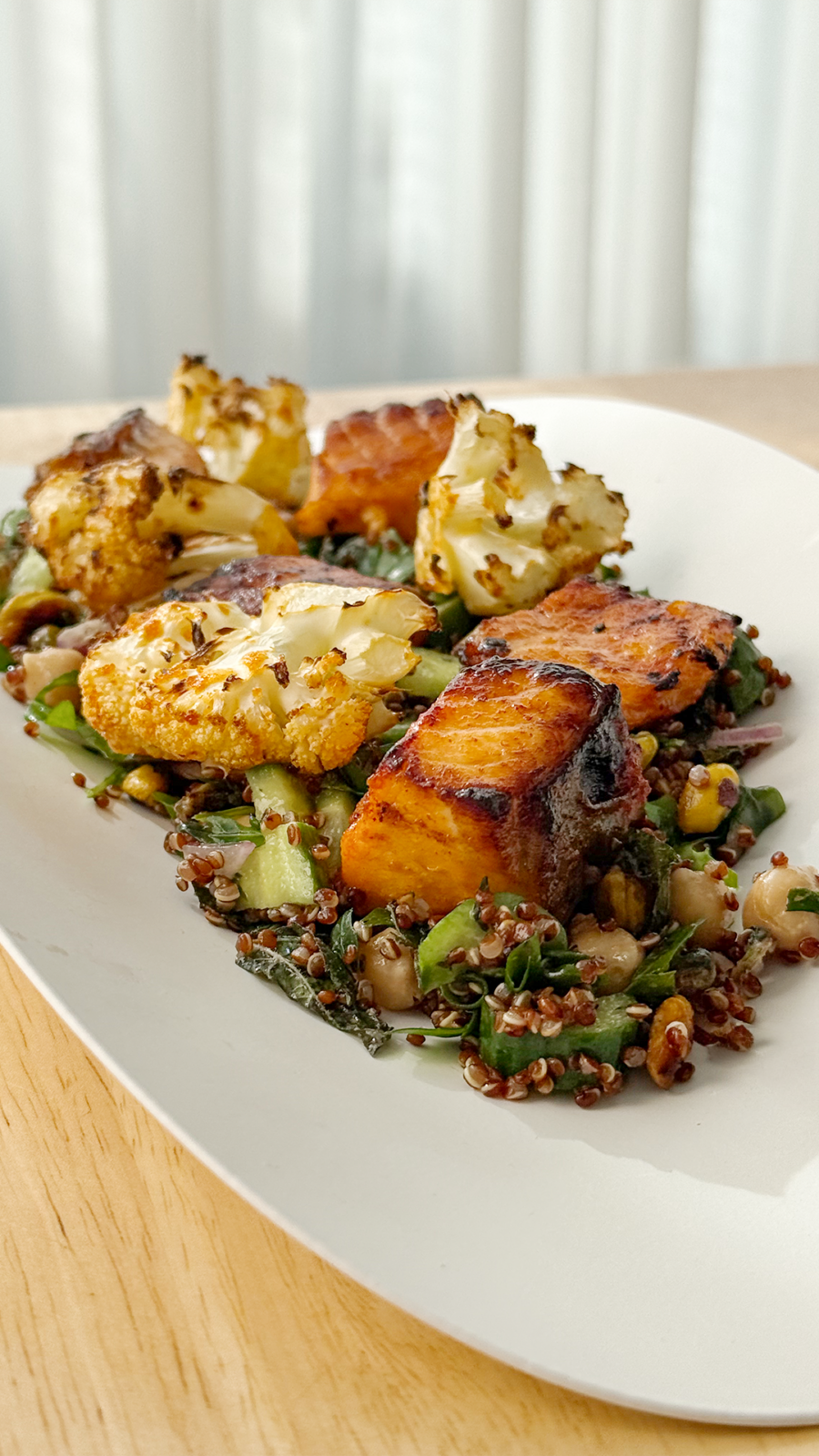 Crispy air-fried salmon and roasted cauliflower served over a quinoa and greens salad on a white plate.