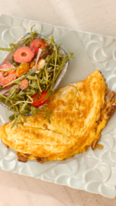 Close-up of a cheesy mushroom omelet with caramelized onions and a colorful arugula salad – healthy and flexible recipe idea